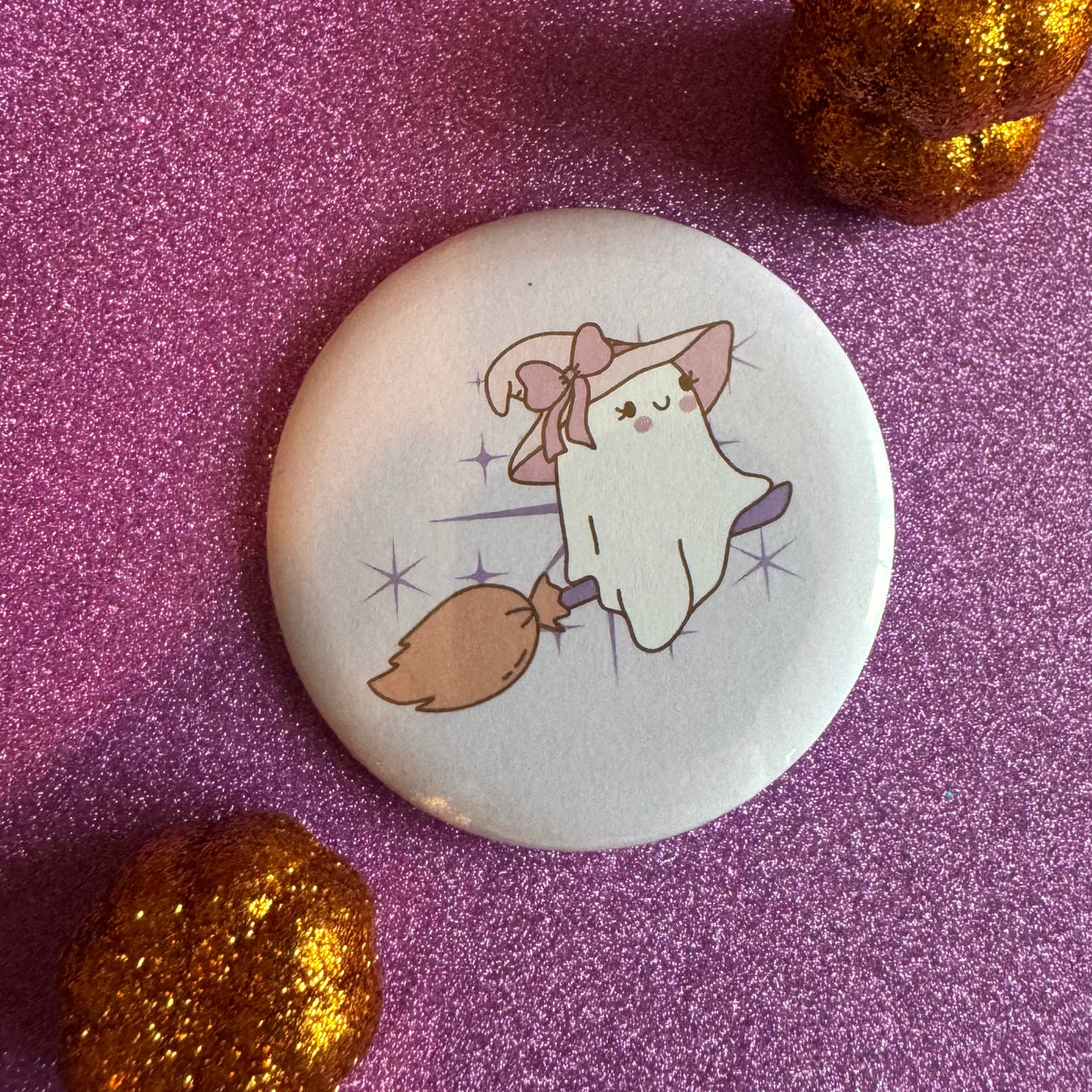 Witchy ghost on broom badge on a glittery pink background
