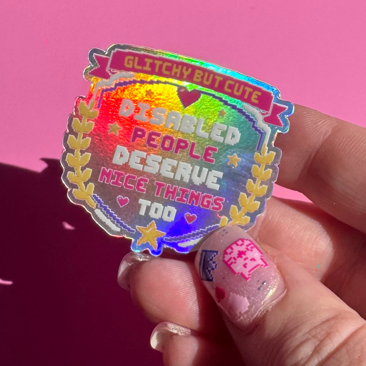 Disabled People Deserve Nice Things Too holographic sticker held between fingers to show its size and rainbow shine