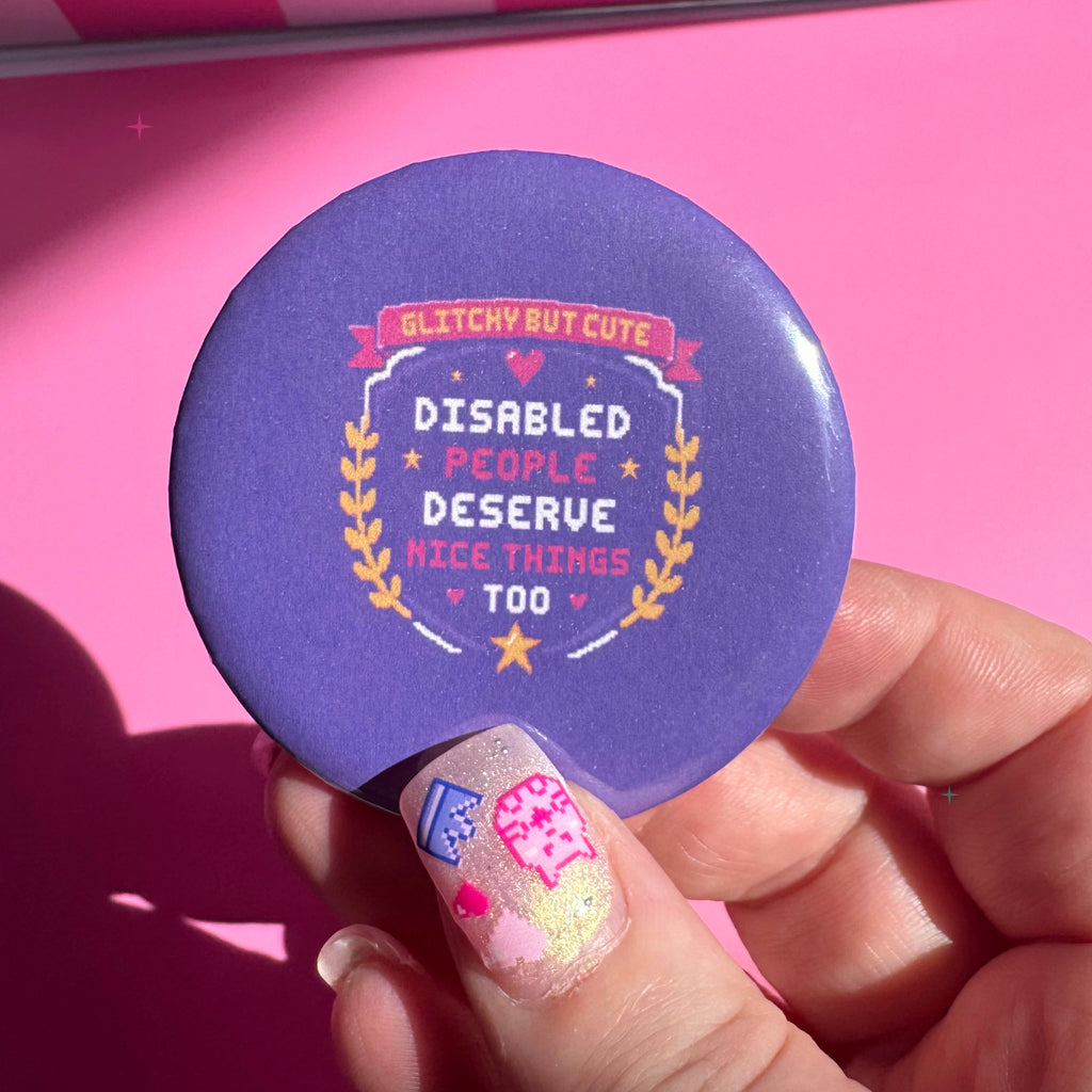 58mm purple Disabled People Deserve Nice Things Too button badge held between fingers for scale