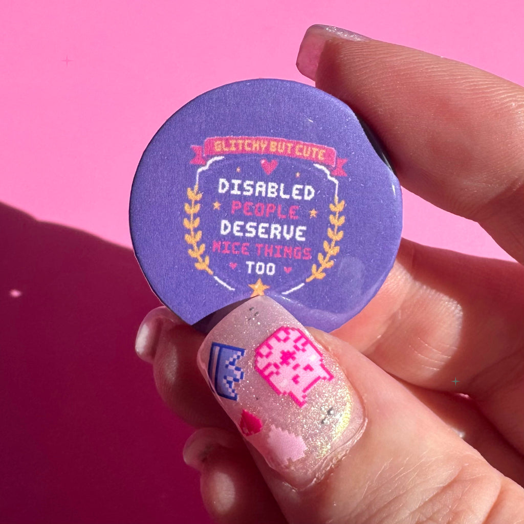 32mm purple Disabled People Deserve Nice Things Too button badge held between fingers for scale