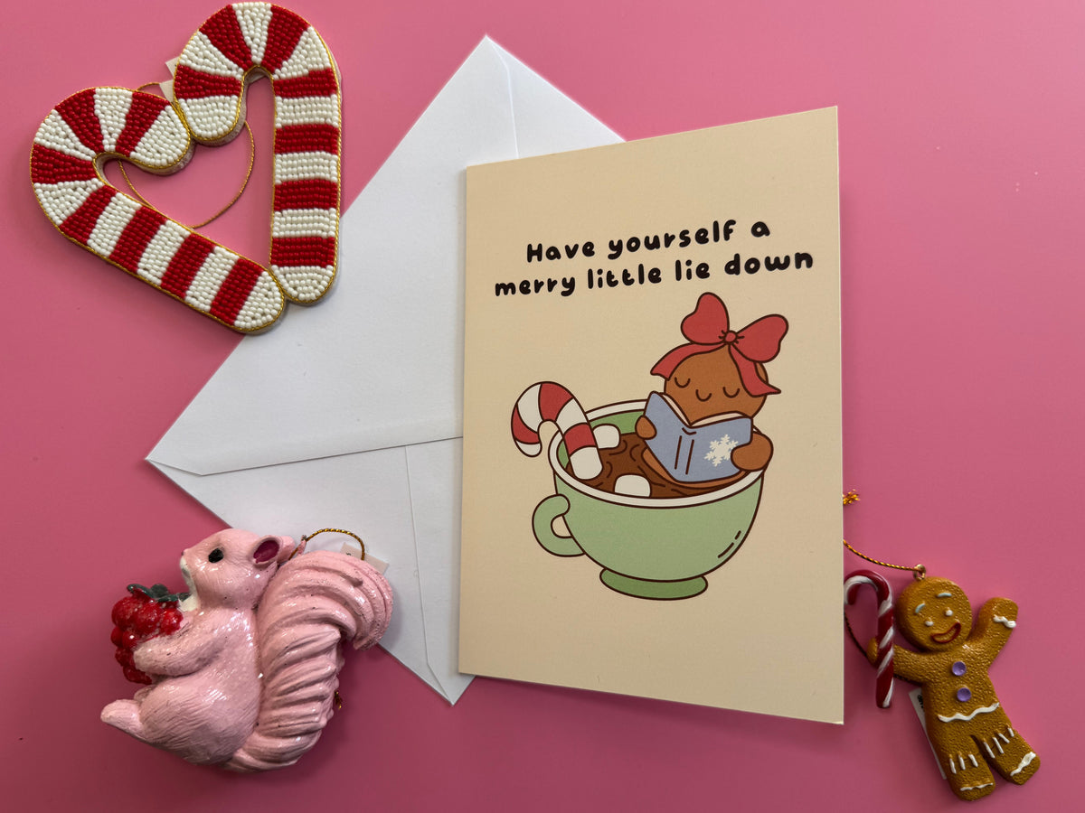 Merry Little Lie Down Christmas card and envelope on a pink background with cute festive decorations.