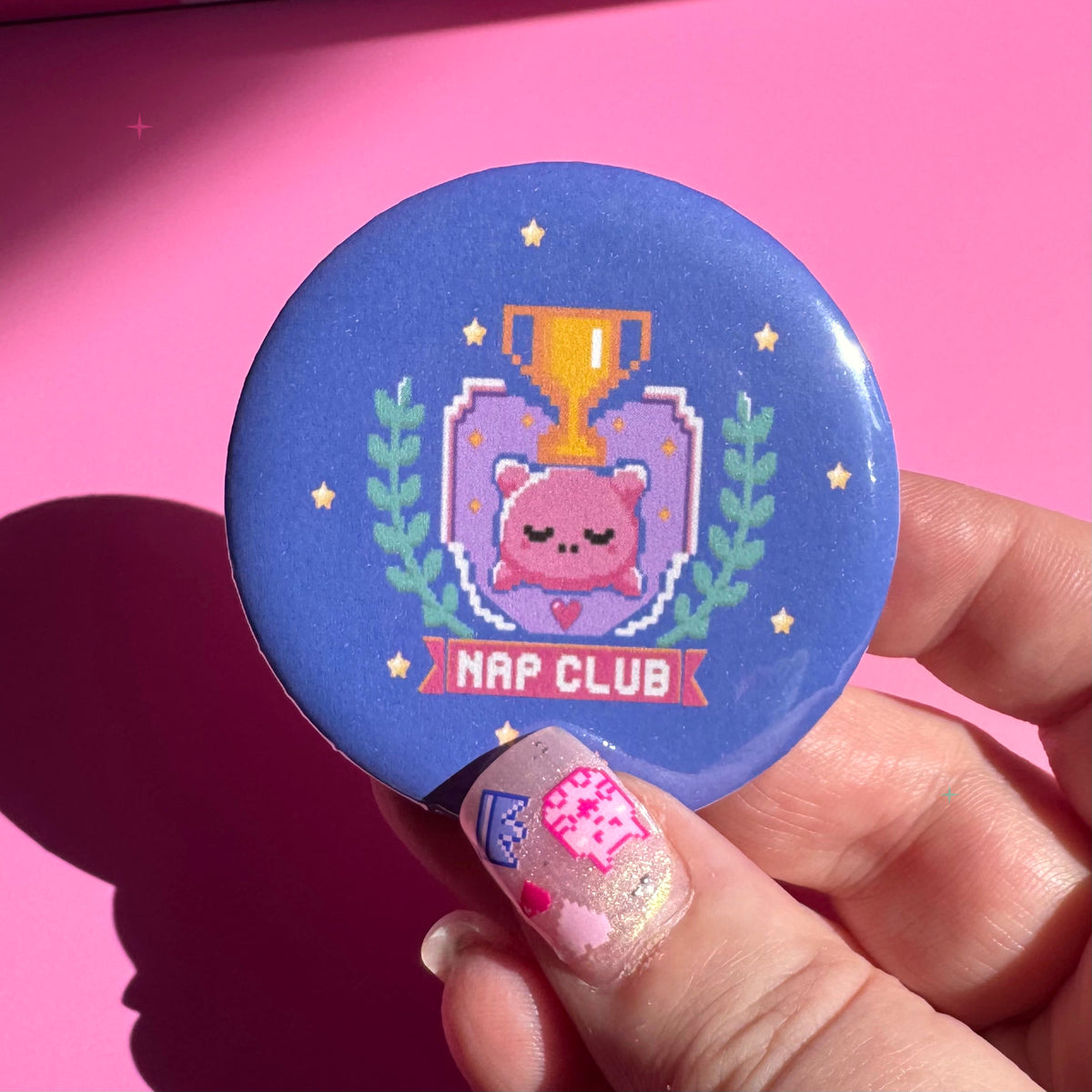 58mm blue Nap Club button badge held between fingers for scale