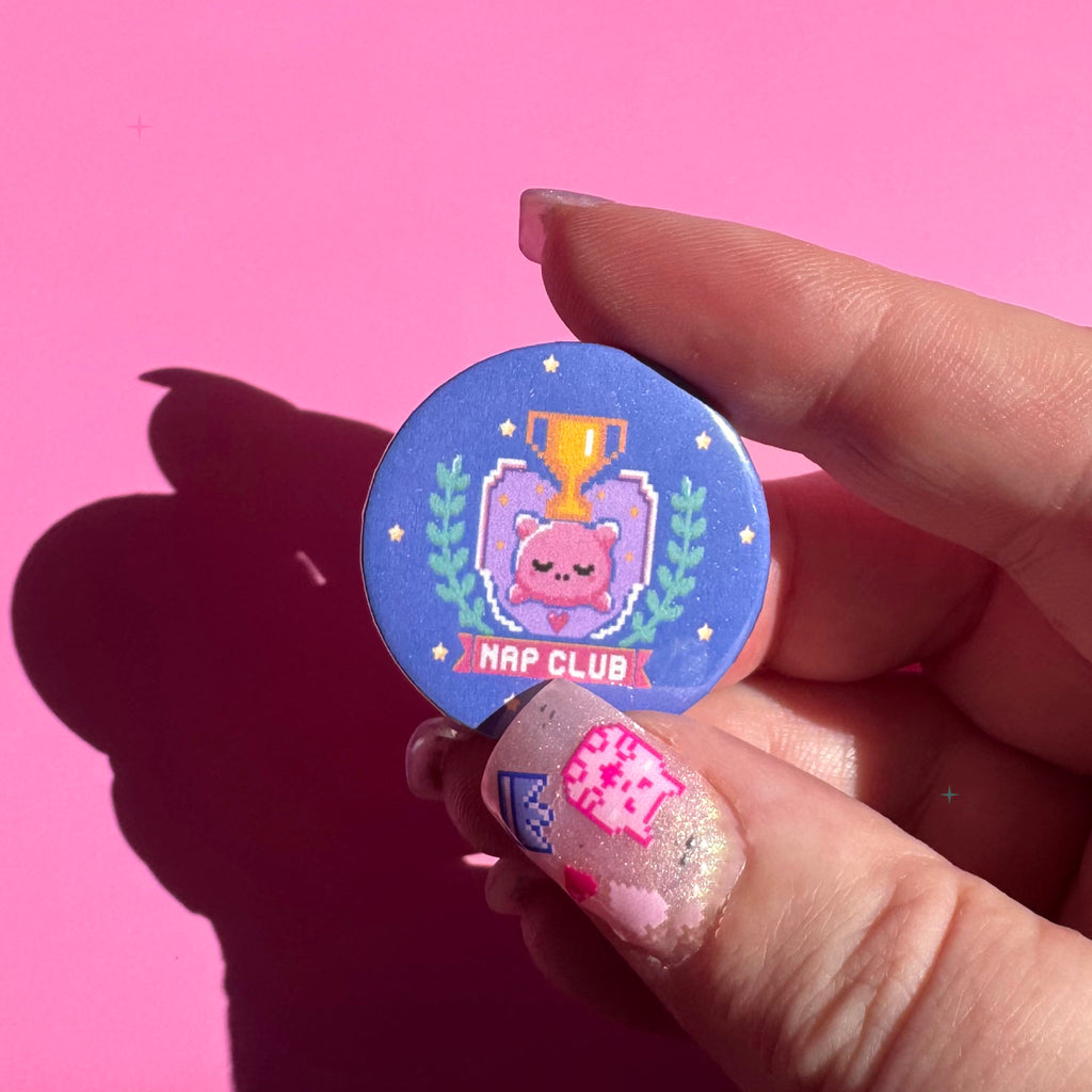 32mm blue Nap Club button badge held between fingers for scale