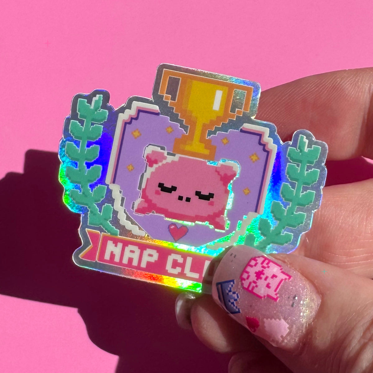 Nap Club holographic sticker held between fingers to show its size and rainbow shine
