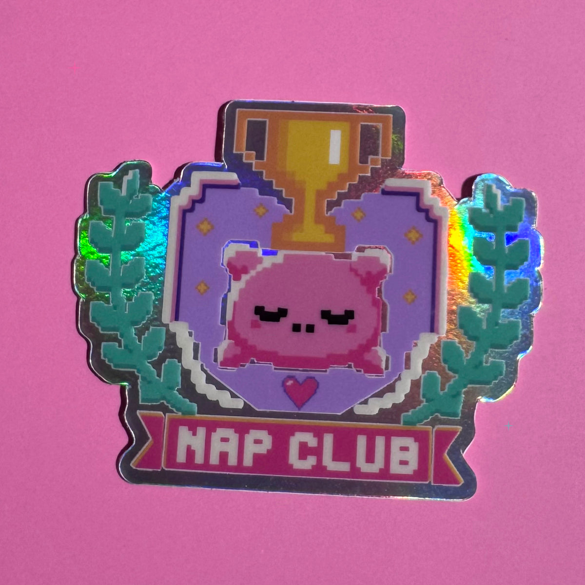 Nap Club holographic sticker with a sleepy pink pillow and gold trophy on a pink background