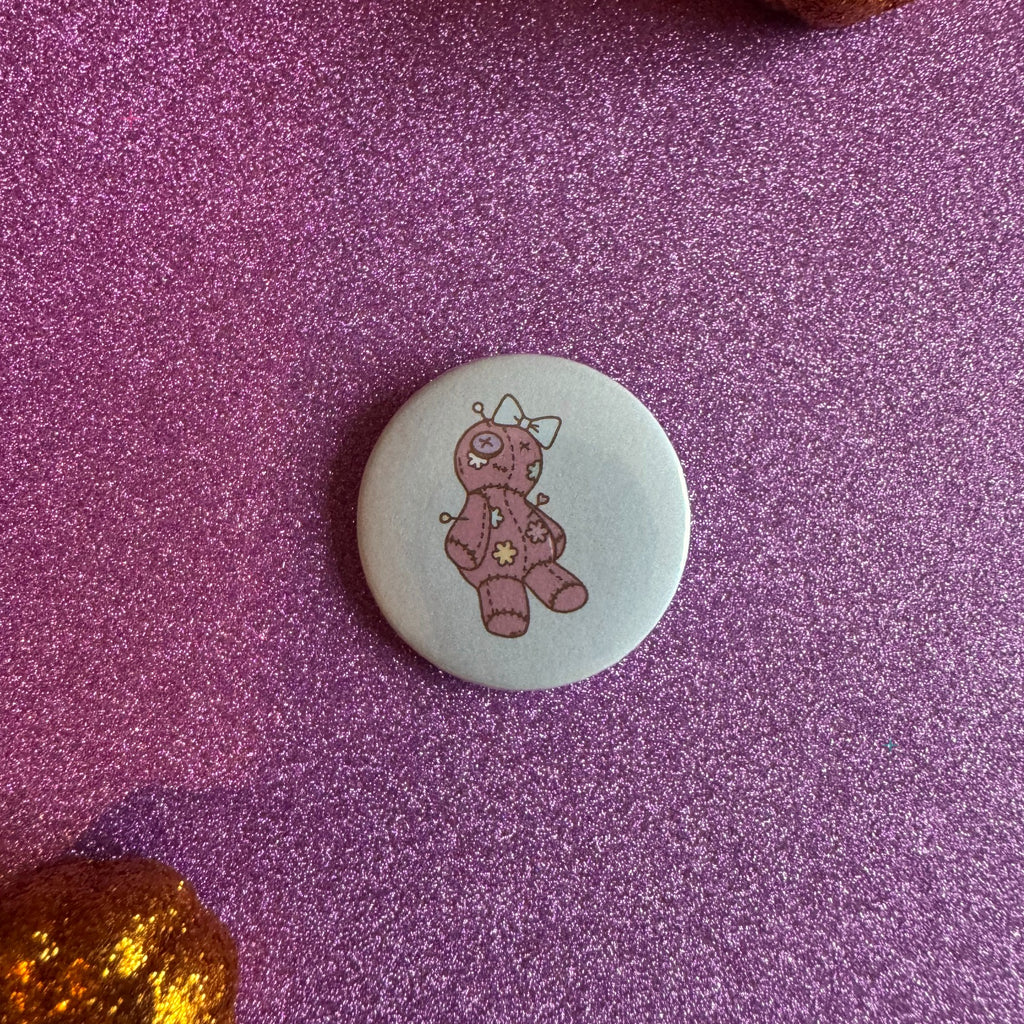 Pink voodoo doll badge on a glittery pink background
