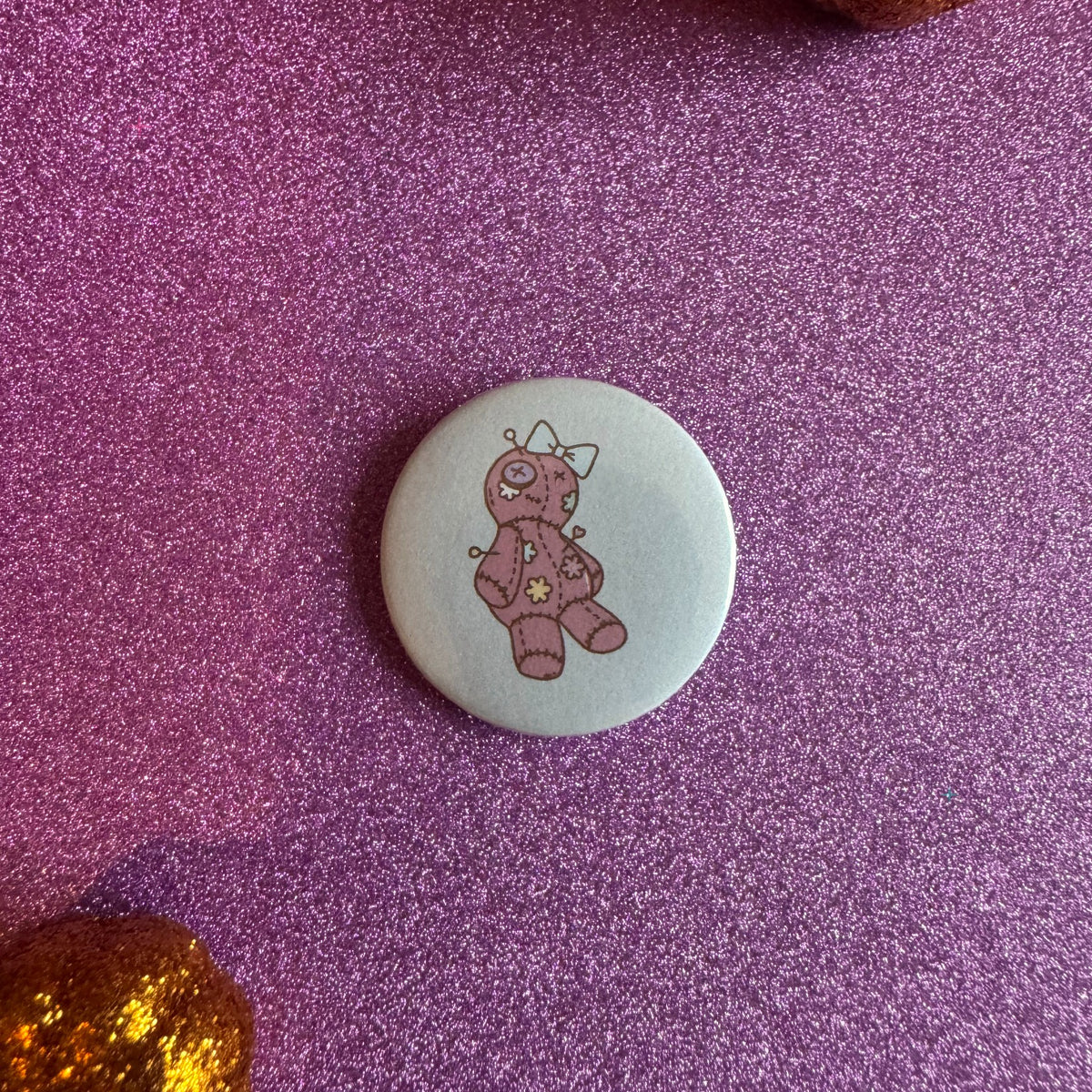 Pink voodoo doll badge on a glittery pink background