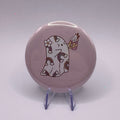 58mm ghost holding a pumpkin spice drink badge on a white background