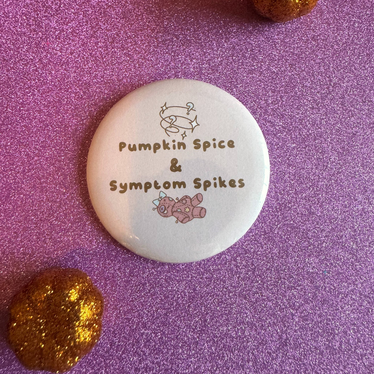 Pumpkin Spice and Symptom Spikes slogan badge on a glittery pink background