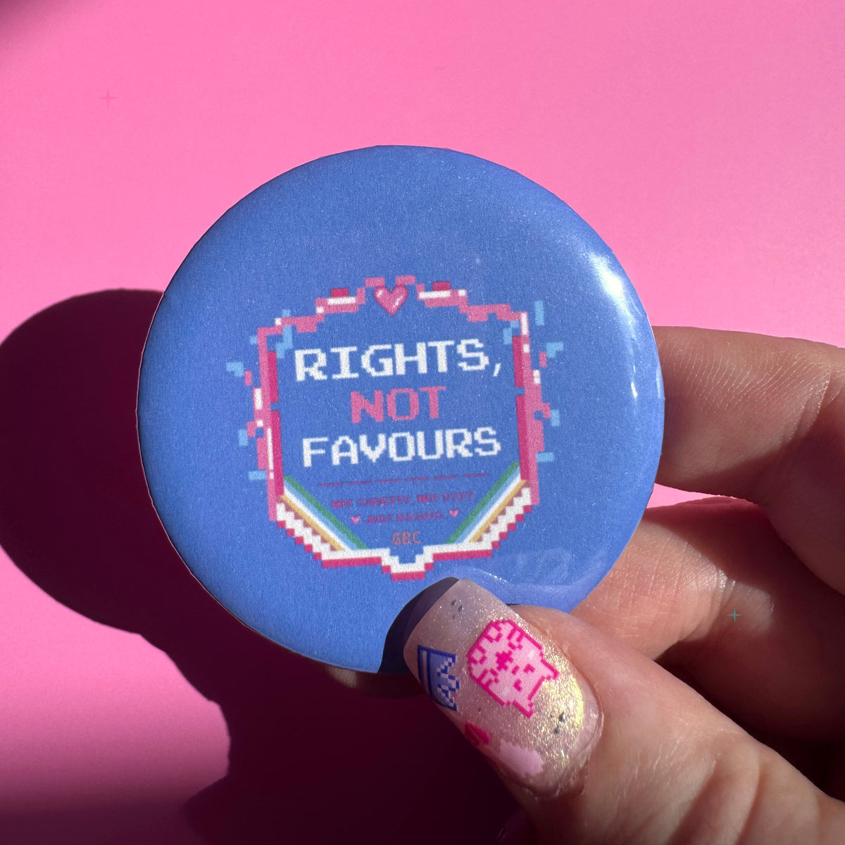 58mm blue Rights, Not Favours button badge held between fingers for scale